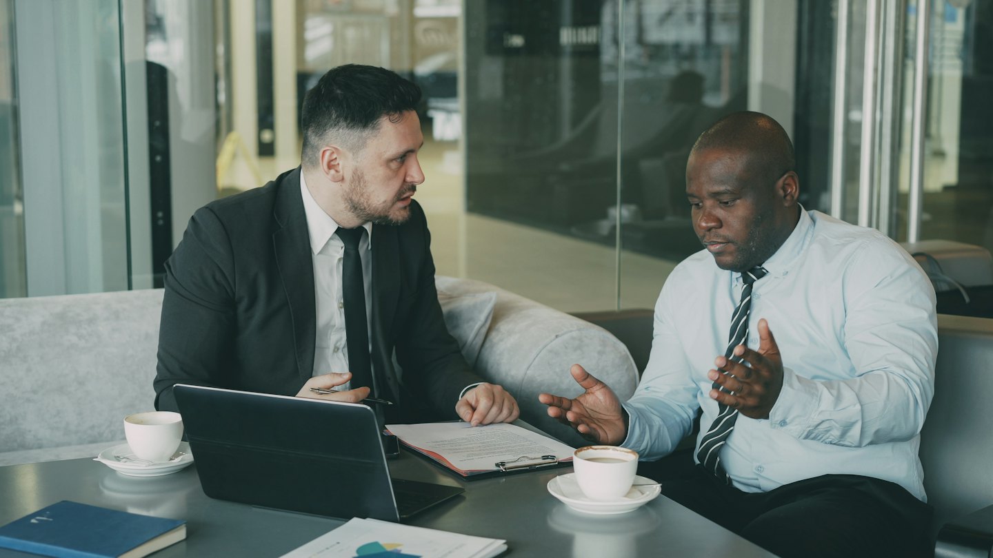 Two businessmen discuss documents at a table.
